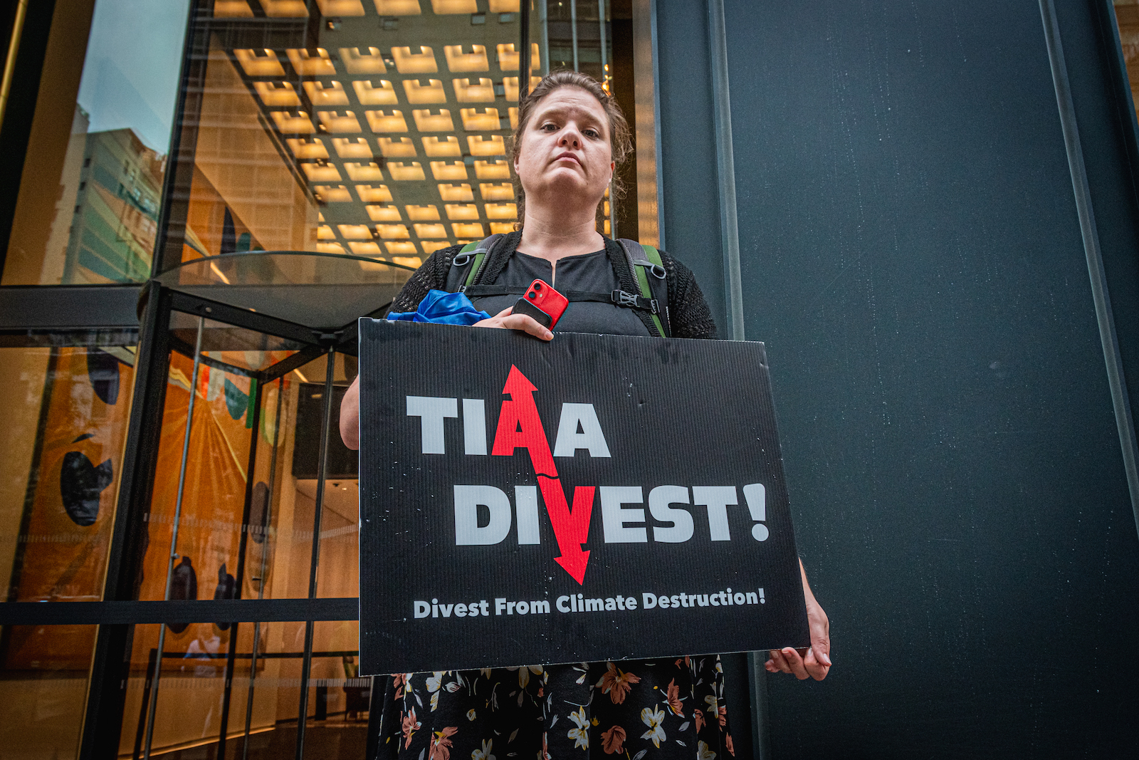 a person holds a sign that says TIAA Divest