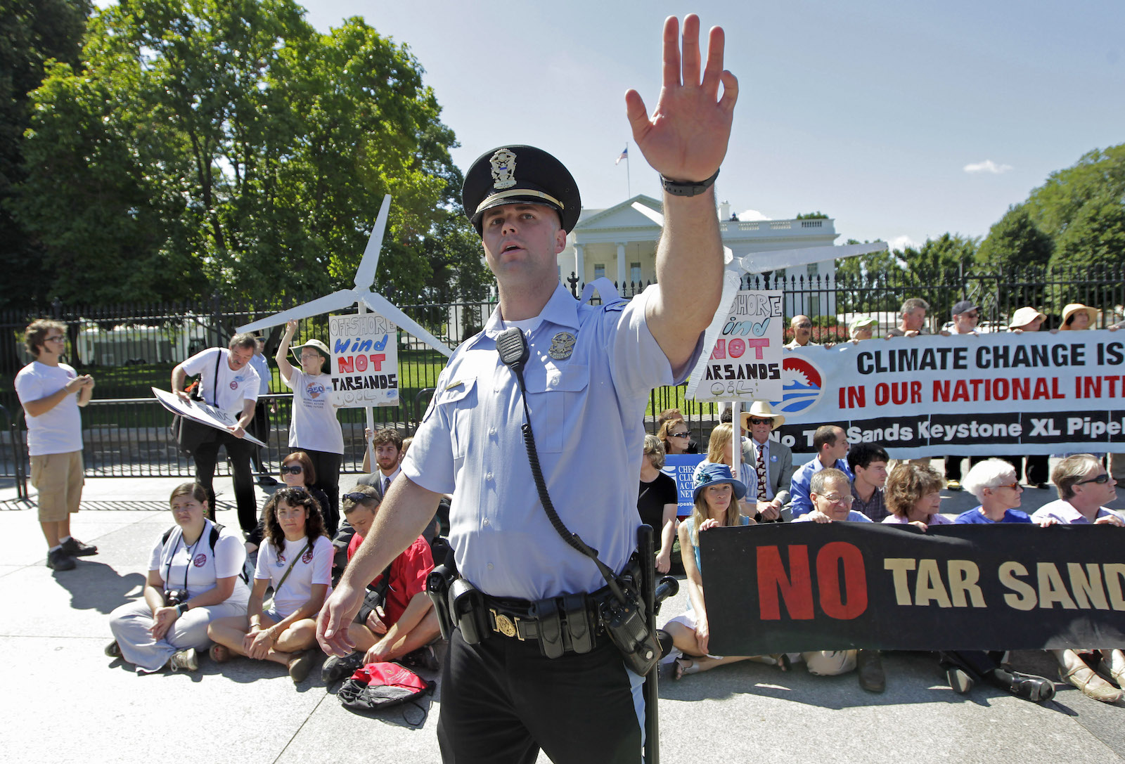 a man in a security or police uniform holds his hand up in front of a gathered group of pipeline protesters