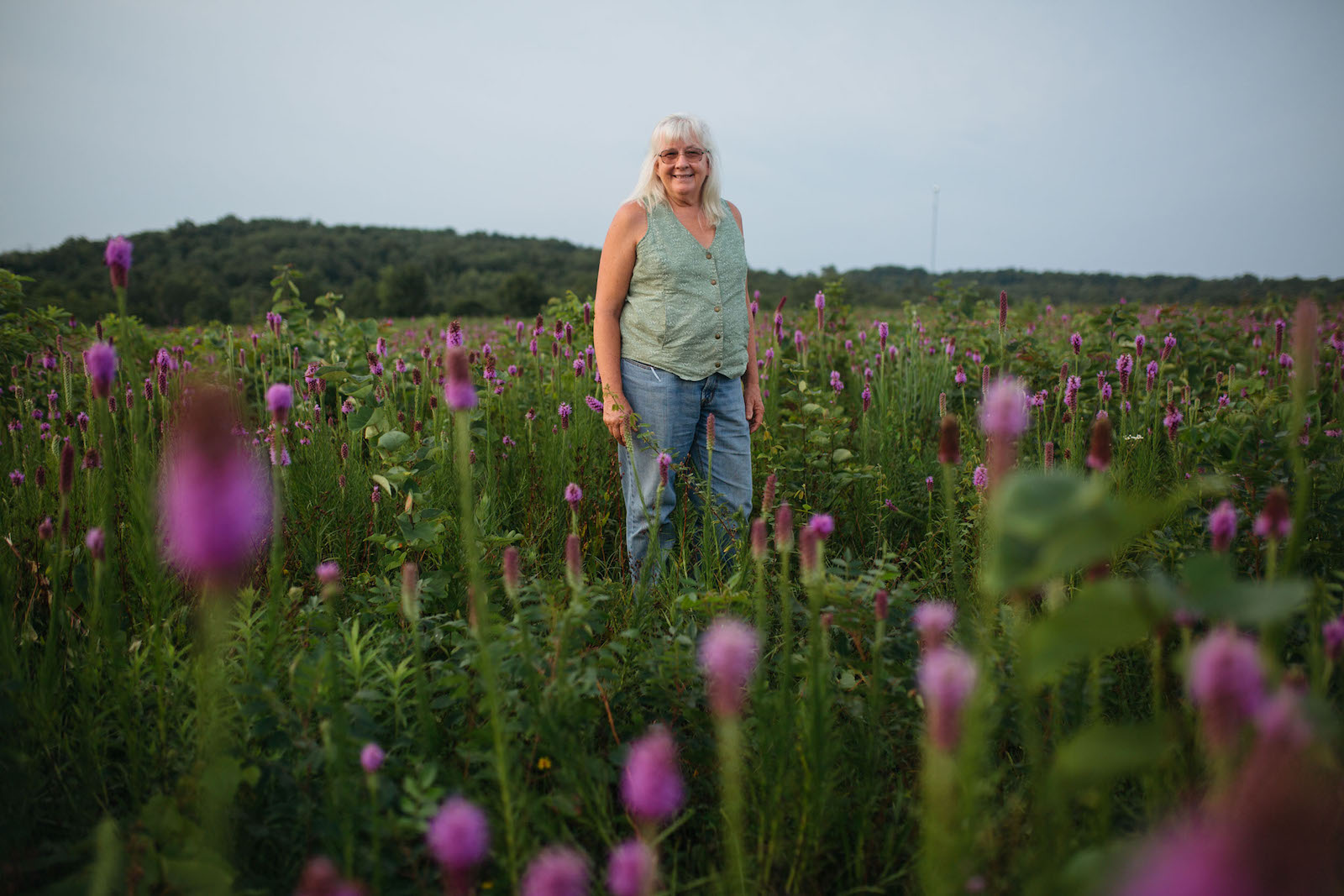 A senior woman stands in a field of purple tall flowers and grass