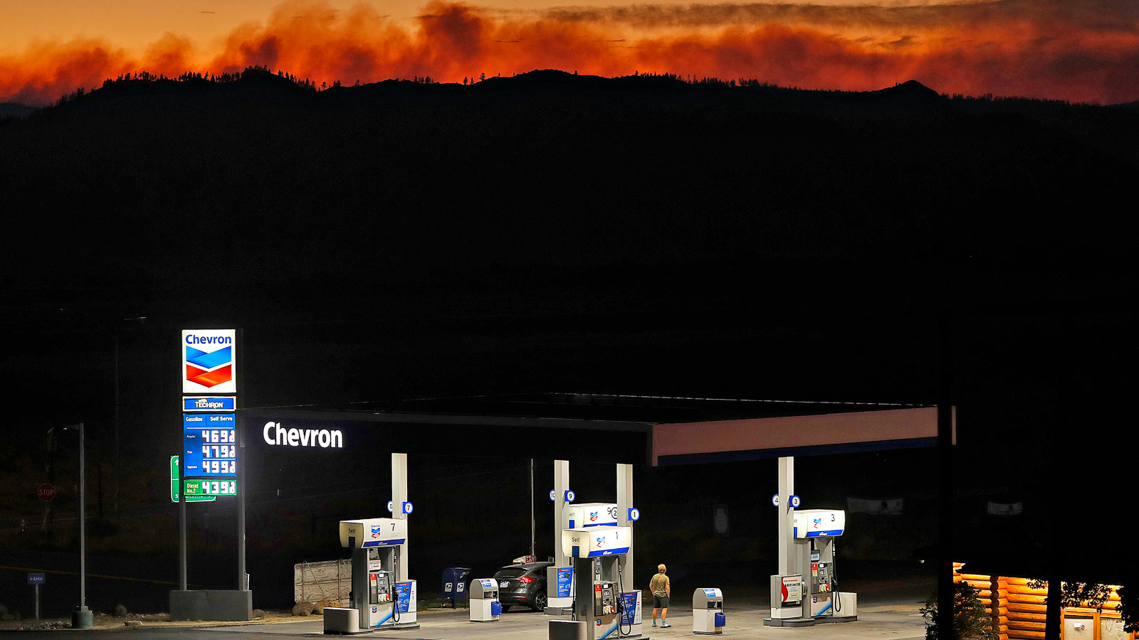 Photo of a Chevron gas station lit up at night in front of an orange, fiery sky