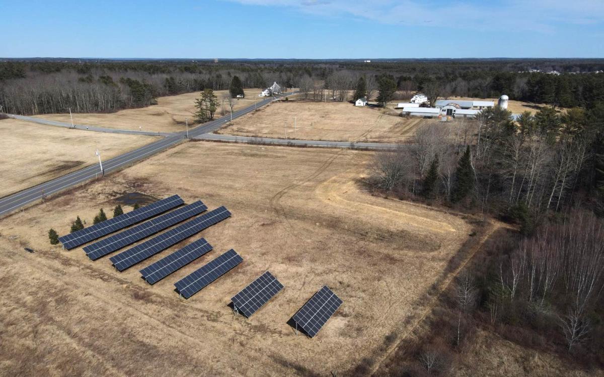 An aerial view of a farm, with seven solar panel installations in a field