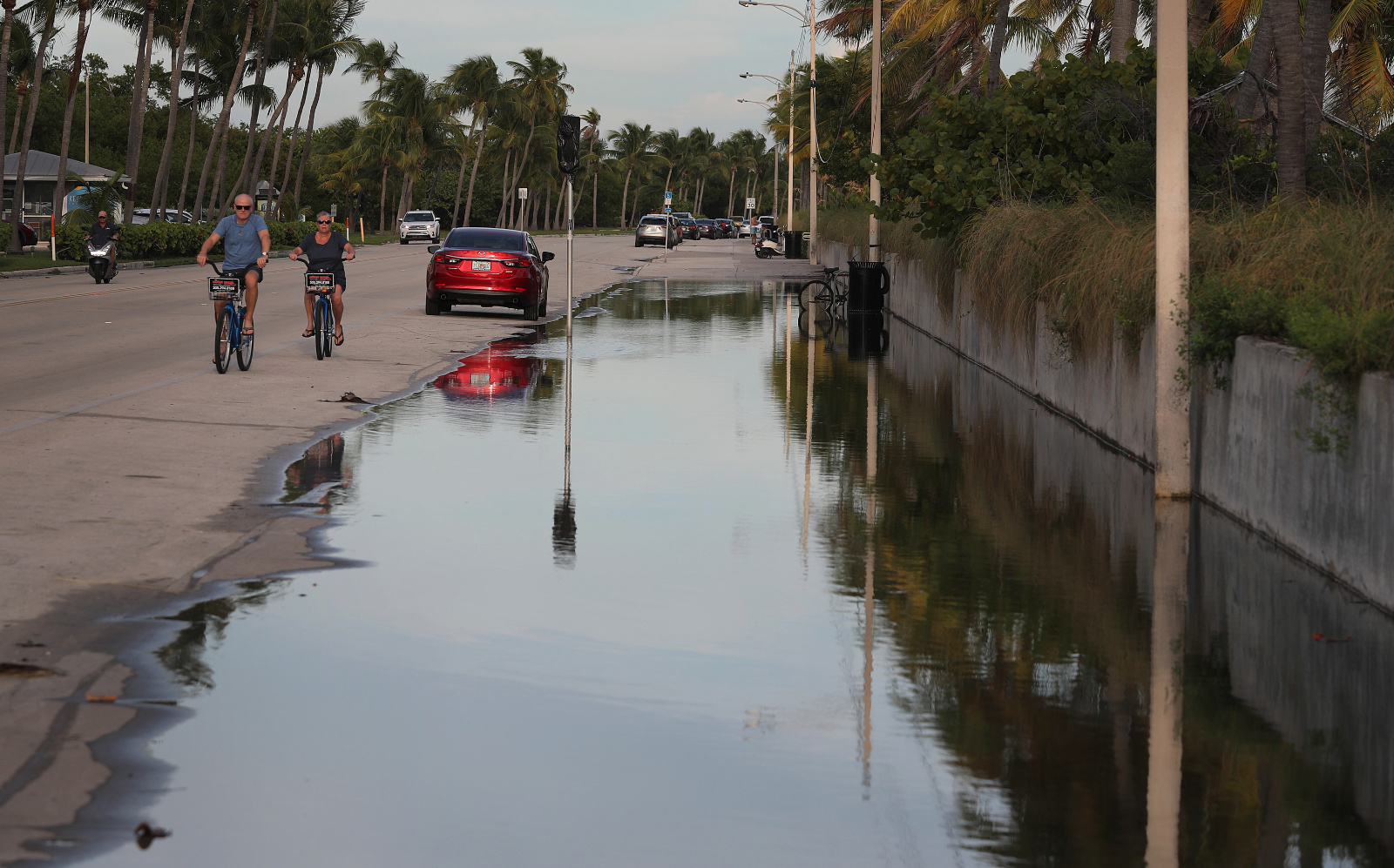 Photo of a flooded street with bikers and palms in the background