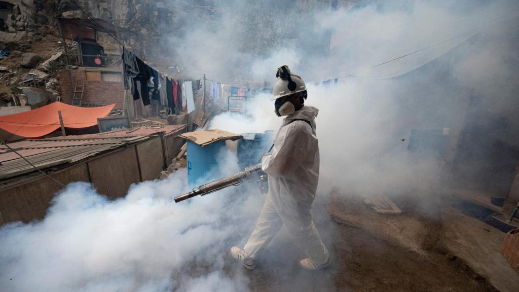A person in protective clothing fumigates a street against the dengue virus
