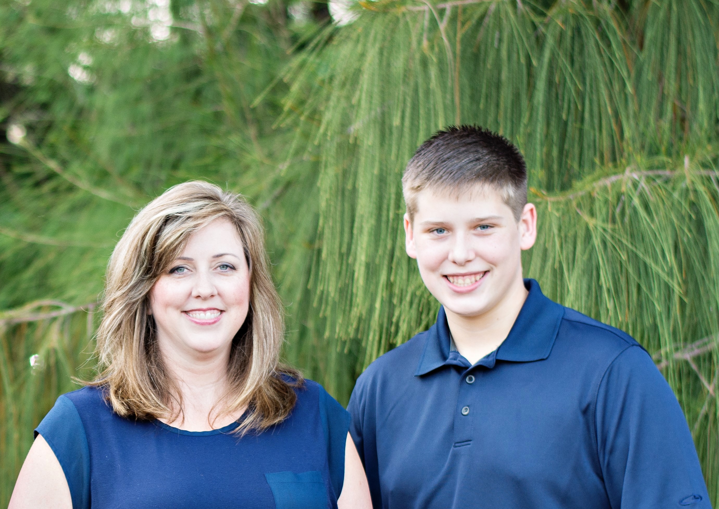 a woman stands next to a teen boy for a family portrait