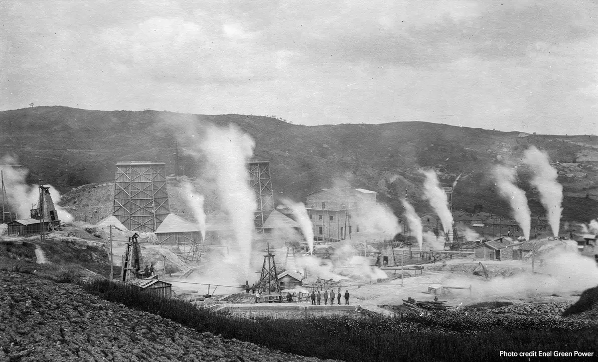 A black and white photo shows smoke rising from an old-fashioned industrial site.