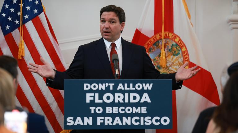 Photo of Ron DeSantis giving a speech. A sign on the podium says "don't allow Florida to become San Francisco"