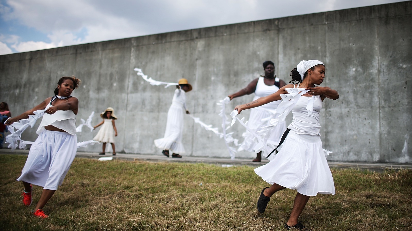 Four Black dancers with the Gallery of the Streets troupe dance in front of a repaired levee in New Orleans, Louisiana.