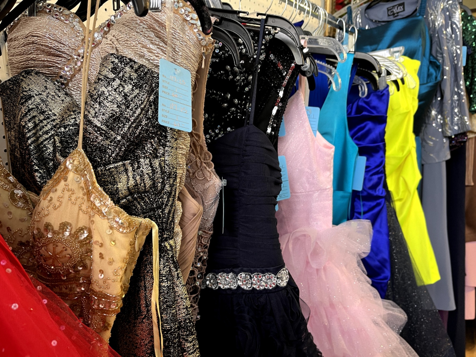 A row of secondhand formal dresses hang on a clothing rack in a store.