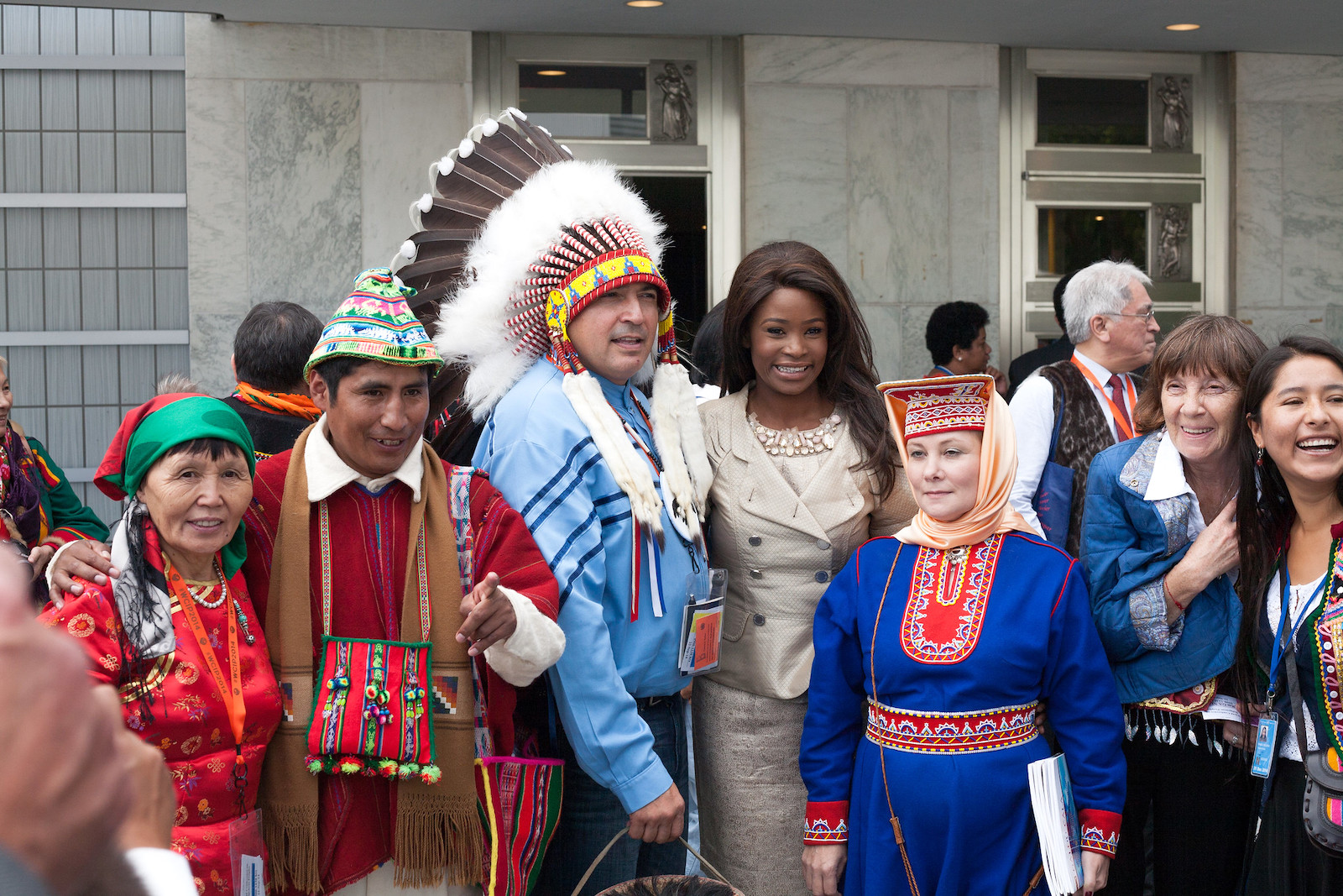 A group of people in front of a building. Many of the people are in traditional Indigenous outfits.