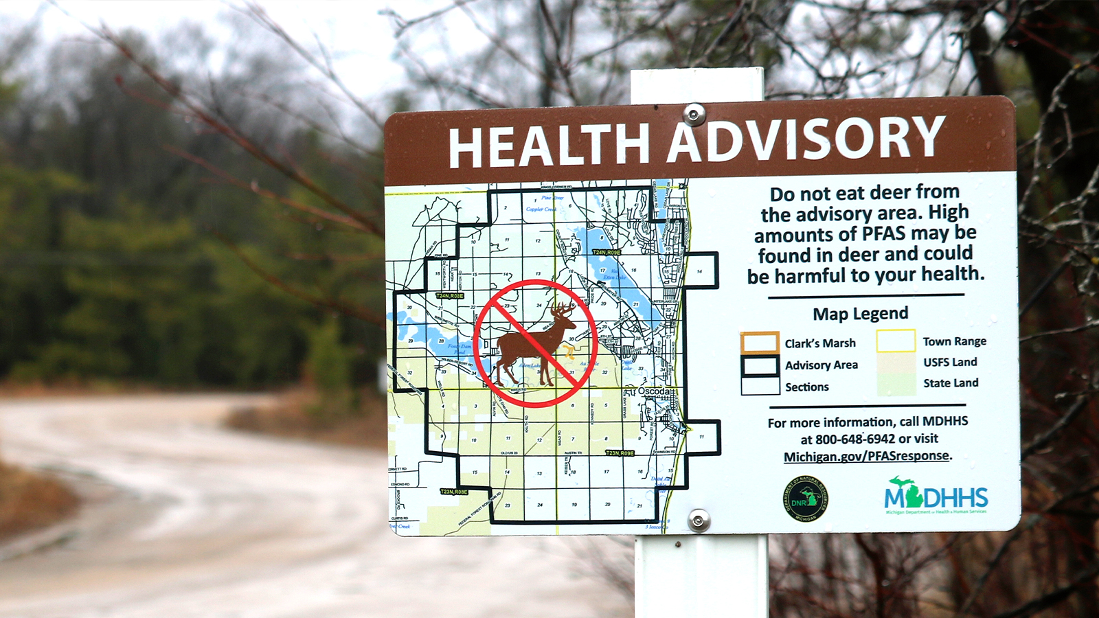 a health advisory sign says "do not eat deer from the advisory area. high amounts of pfas may be found in deer and could be harmful to your health" while showing a map of the surrounding are.