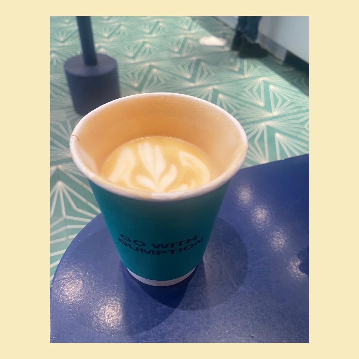 A half-drunk latte in a teal paper cup sits on a blue table