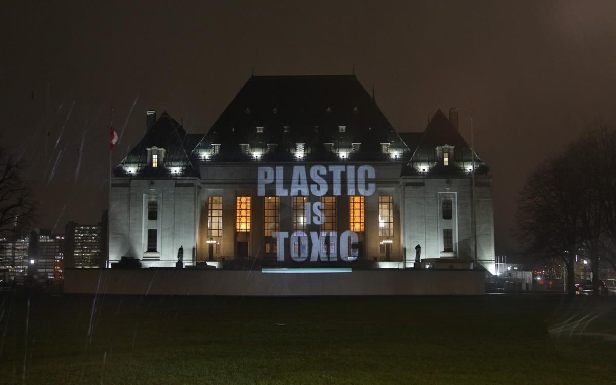A view of Canada's Supreme Court building at nighttime, with large capital letters shining on it, spelling out "PLASTIC IS TOXIC"