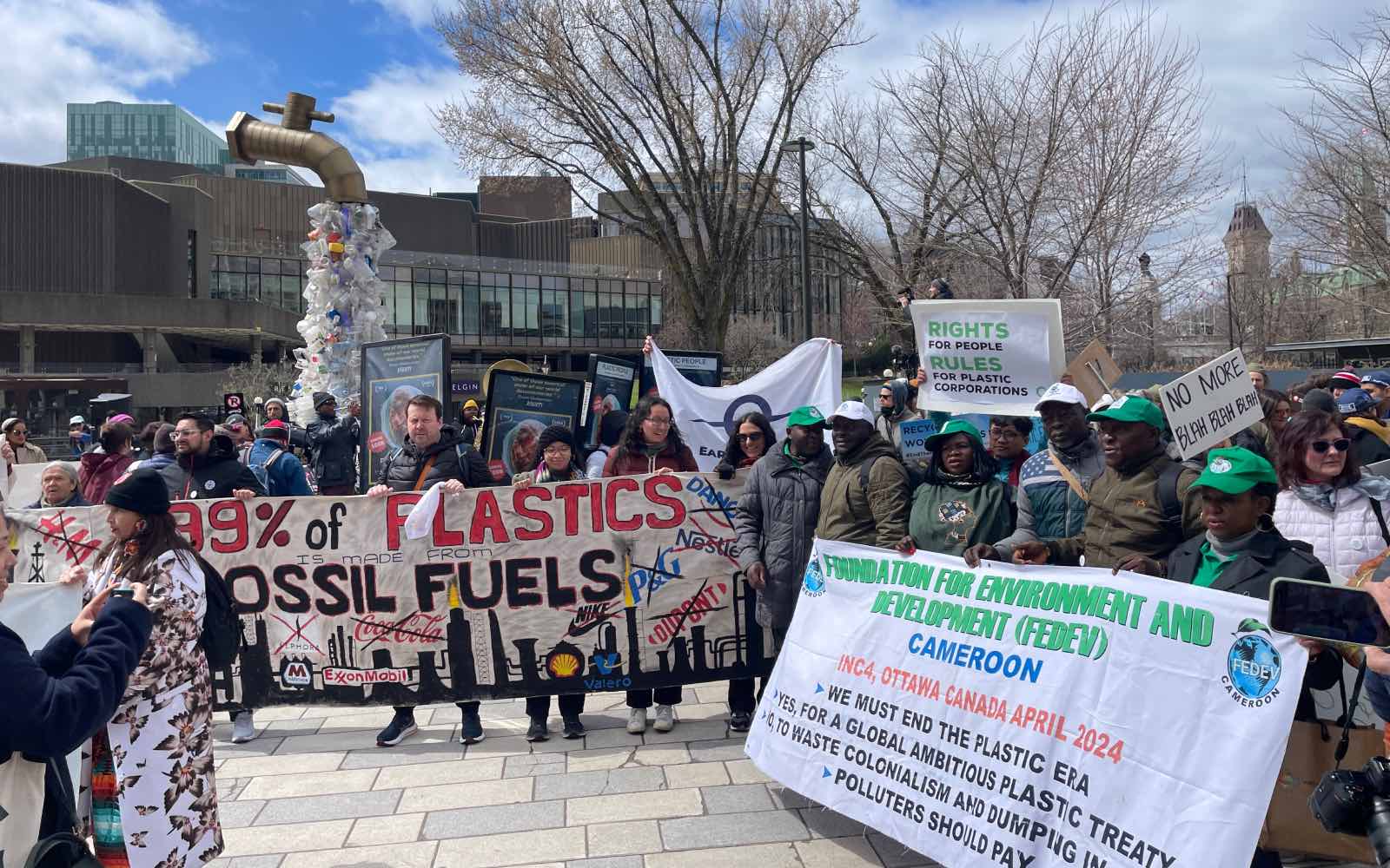 A crowd of people hold up large banners and signs showing anti-plastic slogans