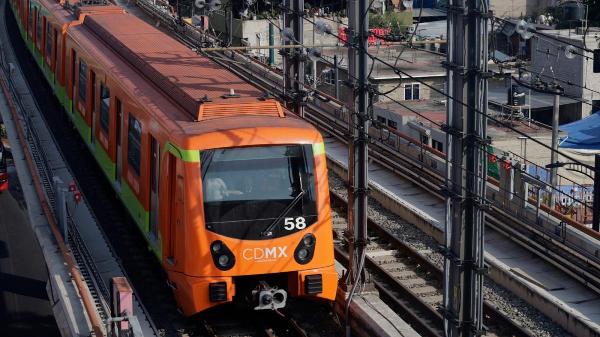 An orange train rolls on a track in a dense city.