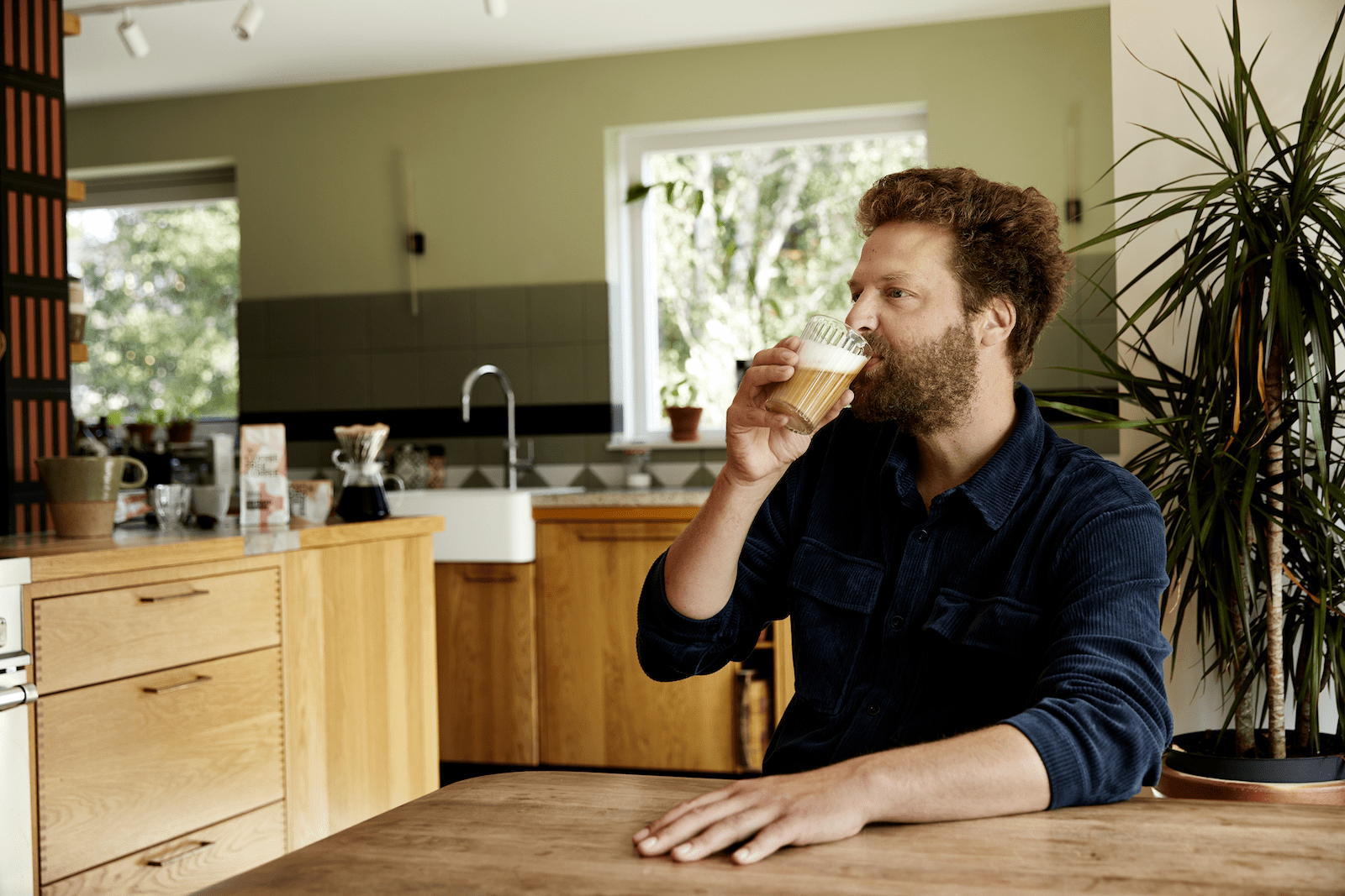 a bearded man drinks coffee from a glass in a nice kitchen