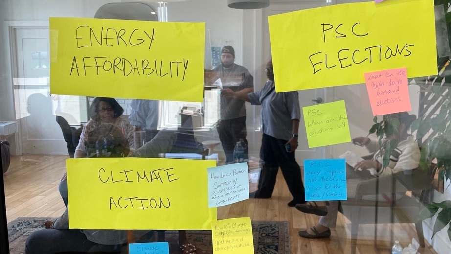 Sticky notes on a glass window that say energy availability and PSC elections as people stand around in the background.