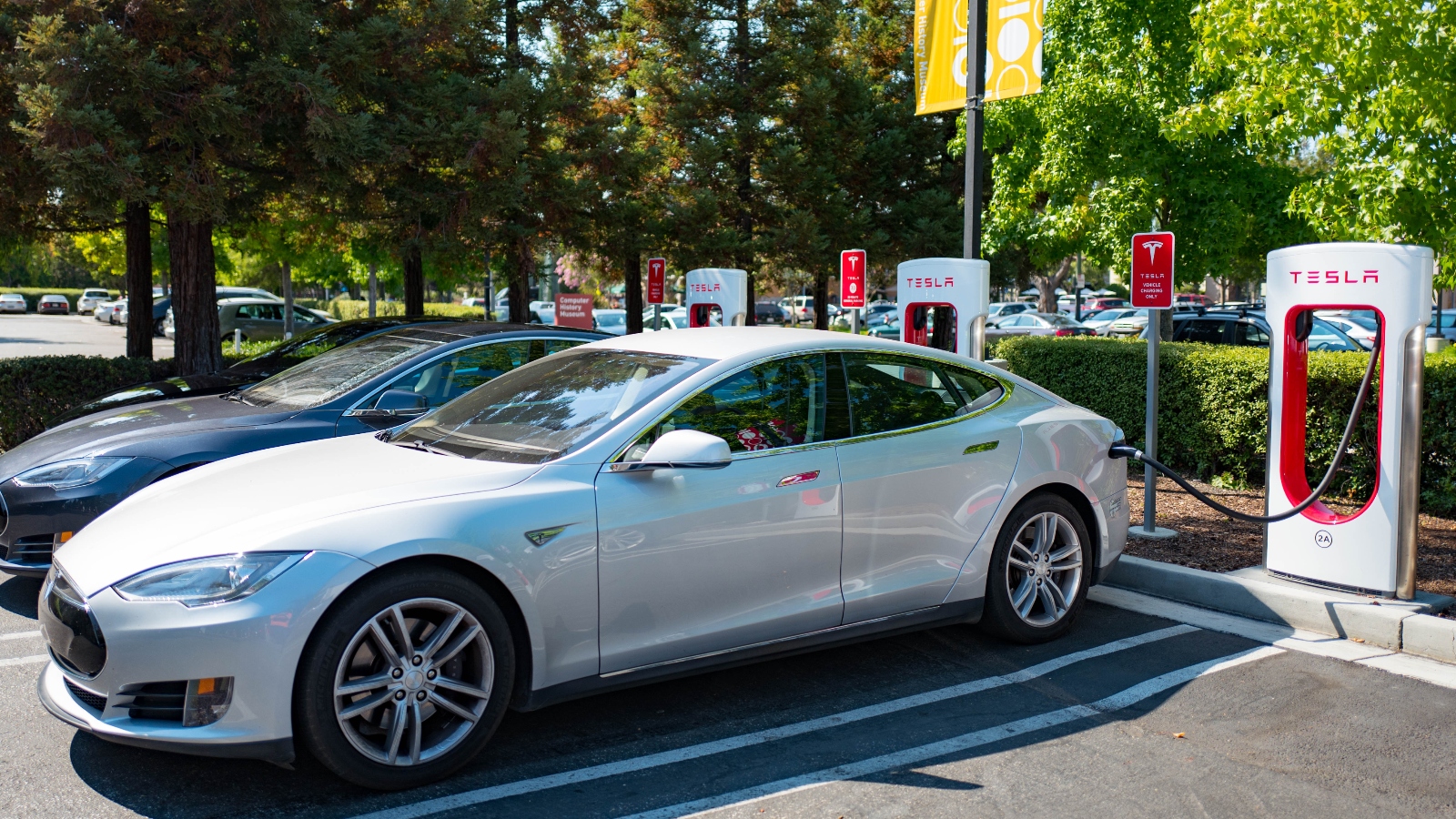 A white car sits in a parking lot attached to a Tesla charger.