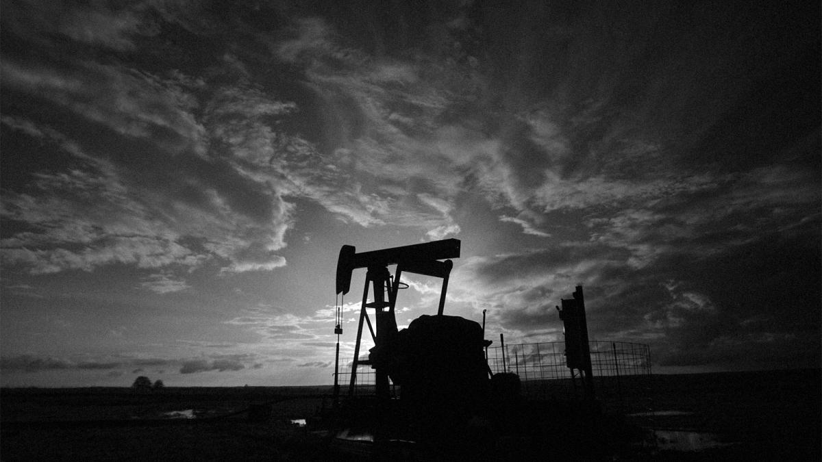 Black and white photo of oil pumpjack silhouetted against a cloudy sky