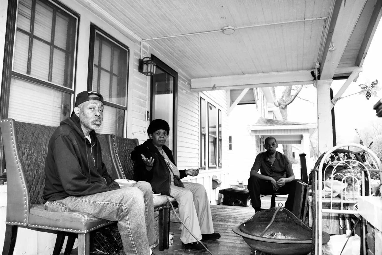 A group of two men and a woman sit on the front porch of a house.
