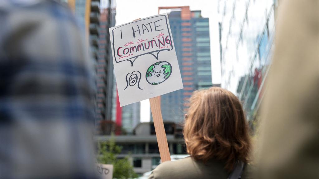 Back view photo of person holding protest sign that reads 'I hate commuting'