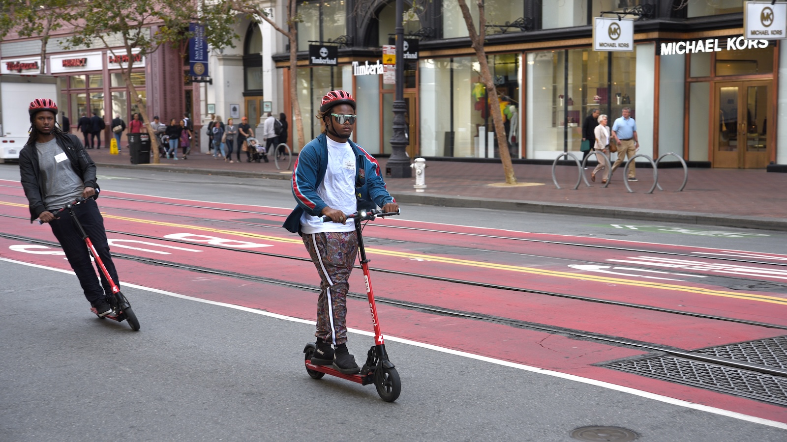 Tourists visiting San Francisco ride their rented Scoot electric scooters down Market Street.