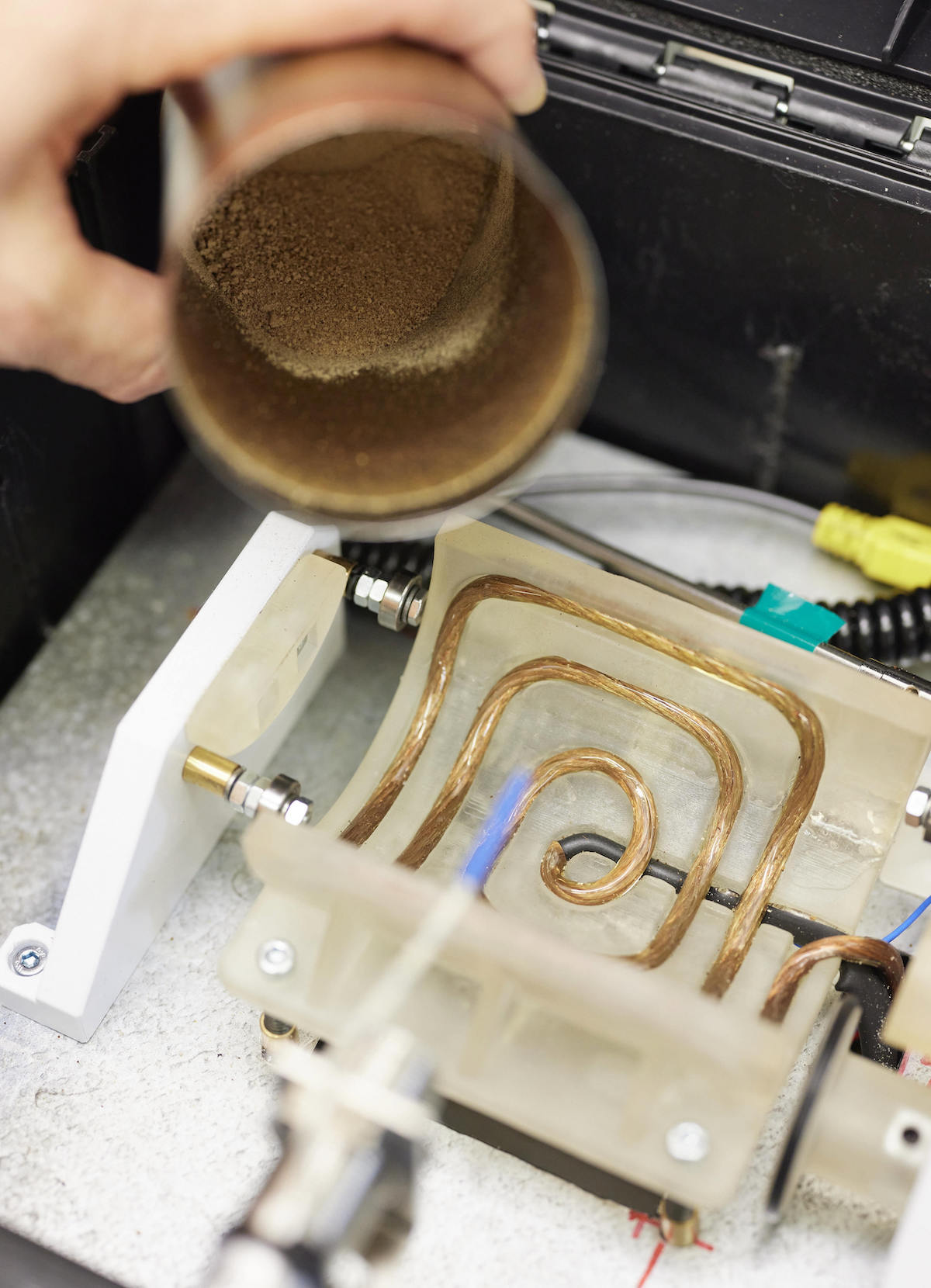 A cup of brown powder hovers over a device with a gold coil