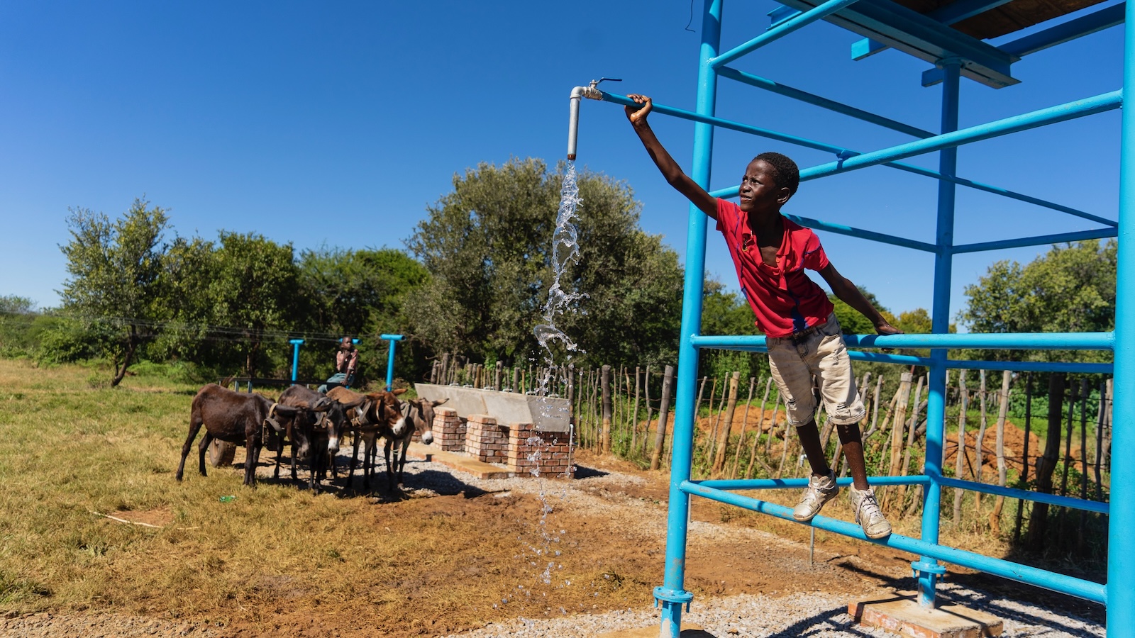 A young boy climbs on a pump assembly as water flows from a spigot in a livestock field in Nyamandlovu, Zimbabwe.