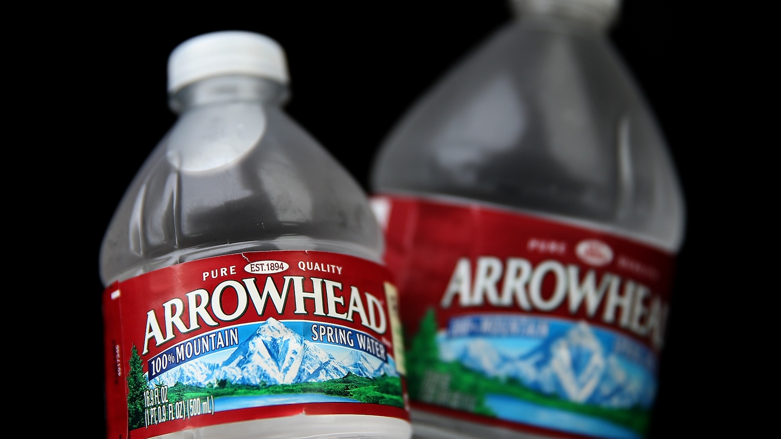 Two bottles of Arrowhead water against a black background. Labels read 100% Mountain Spring Water