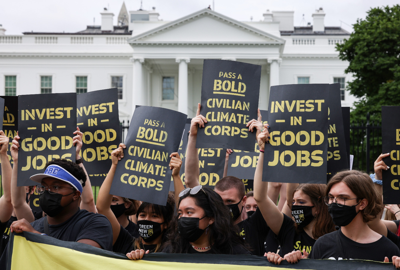 Photo of protesters in front of the White House holding signs reading 'invest in good jobs' and 'pass a bold Civilian Climate Corps'