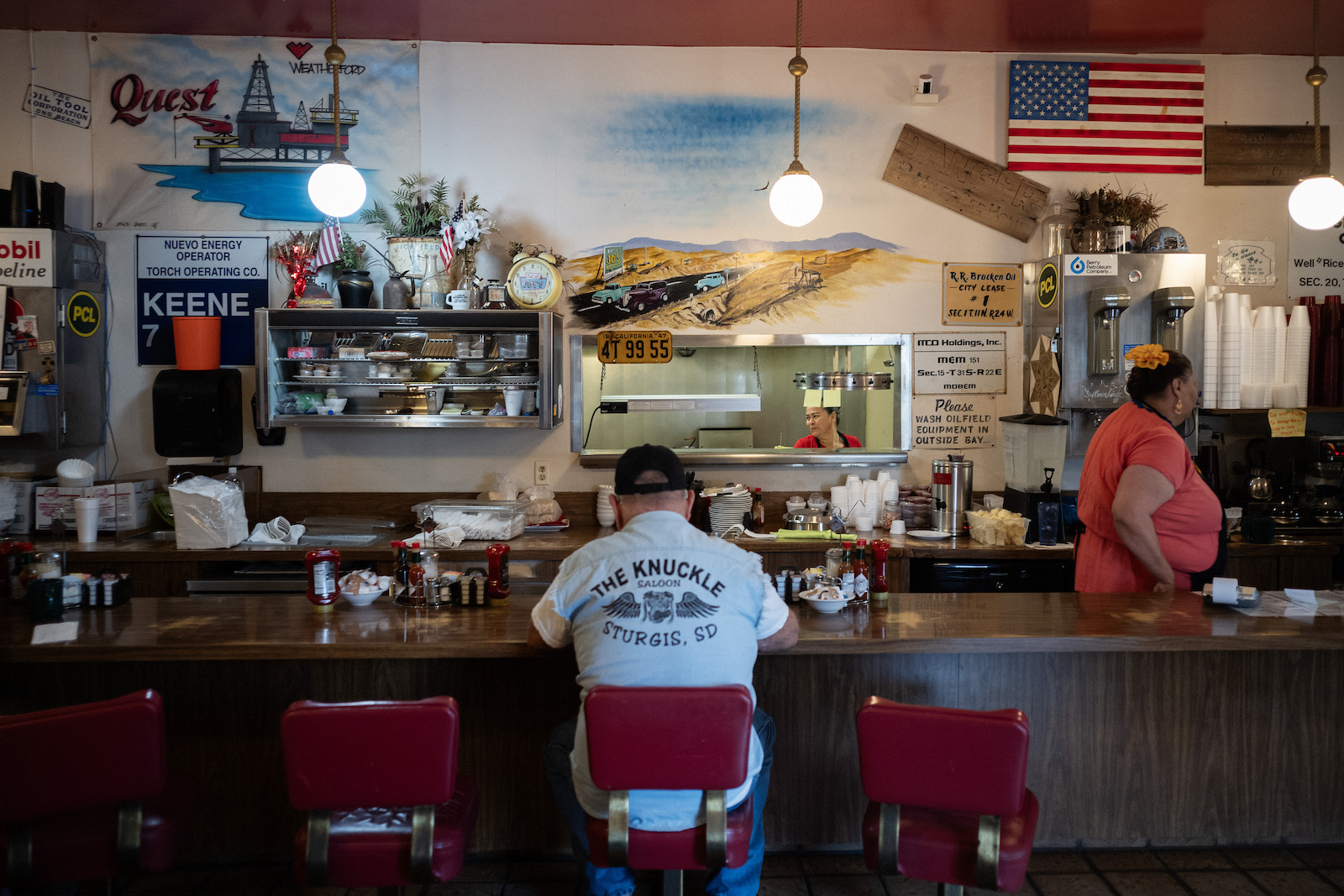 A man sits at a diner counter with oil and gas paraphernalia on the wall