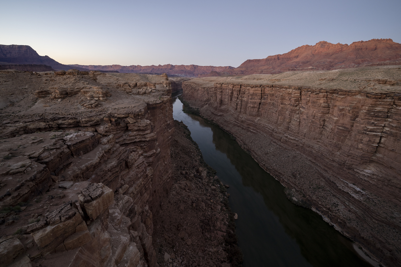 a stream runs through a large red rock canyon at dusk