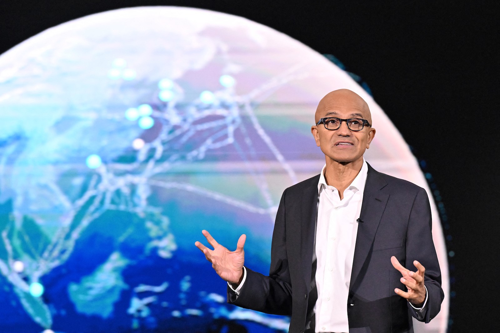 一名身穿西装、戴眼镜的男子在地球图标前讲话