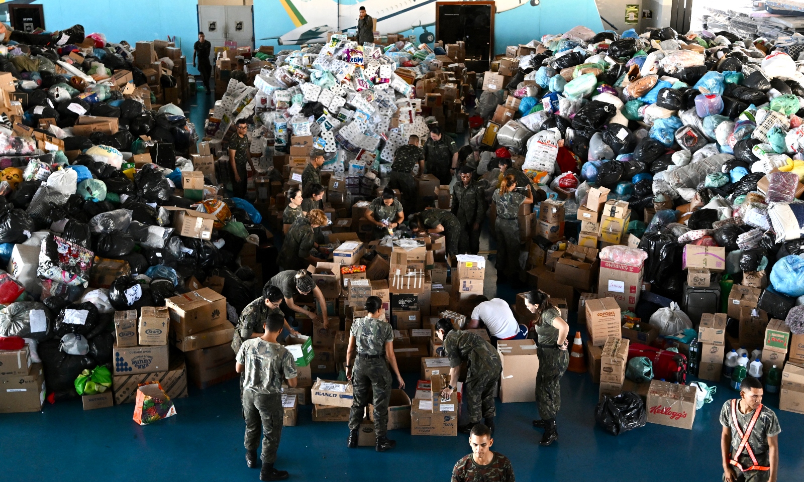 Soldiers in uniform stand in front of a mountain of donated goods in boxes.