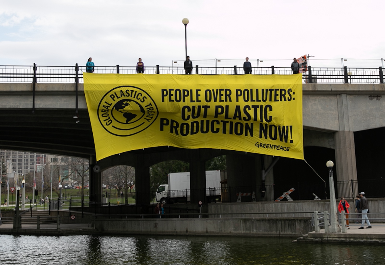 Greenpeace protestors hang a yellow banner that says 'People Over Polluters: Cut Plastic Production Now!' from a bridge