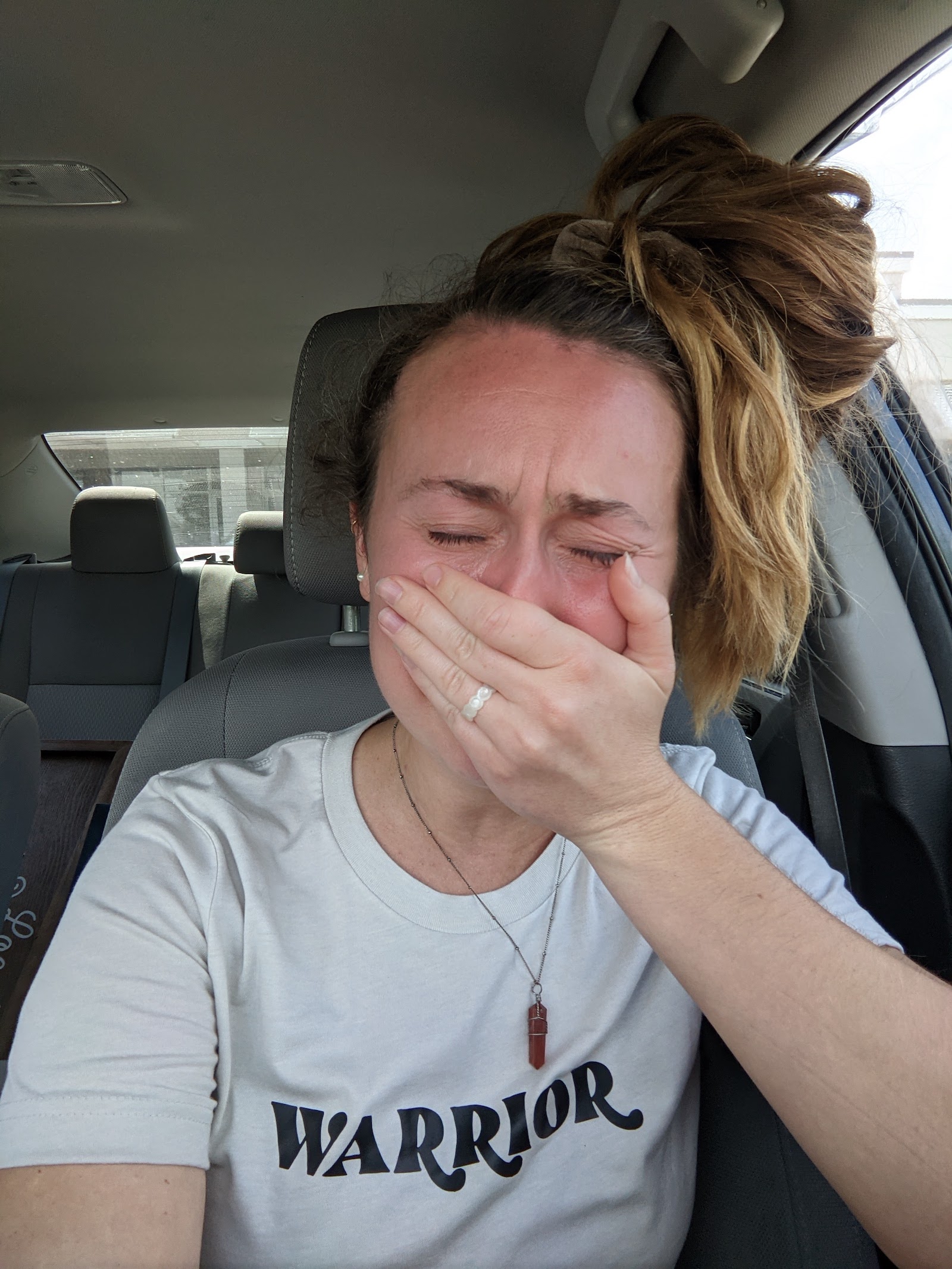 A woman sits in a car crying holding her hand over her mouth
