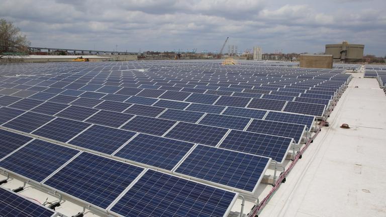 A large array of solar panels stretches over an urban landscape under a cloudy sky.