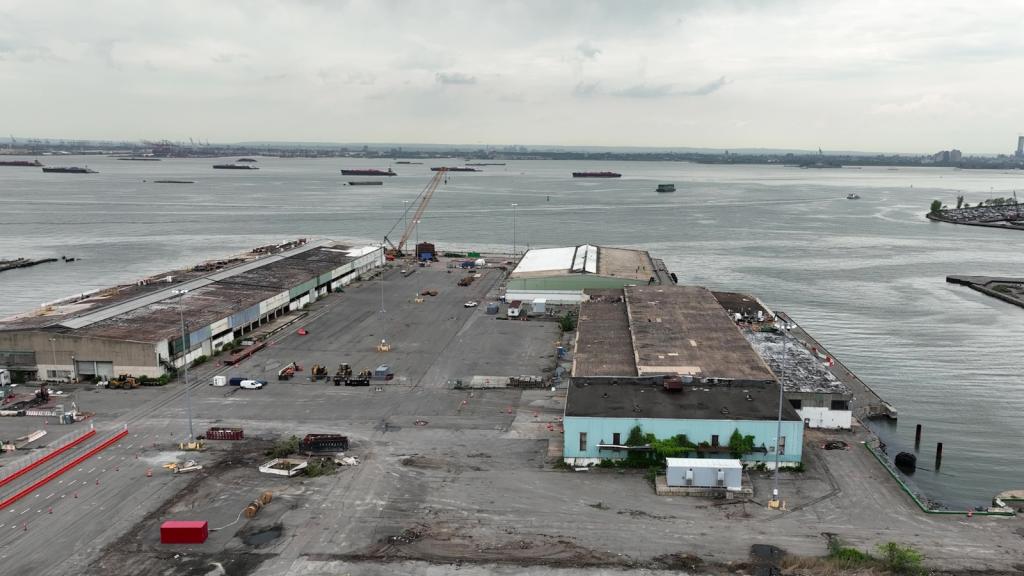 Low warehouse-like buildings sit in a parking lot on the end of a bay under a gray sky.