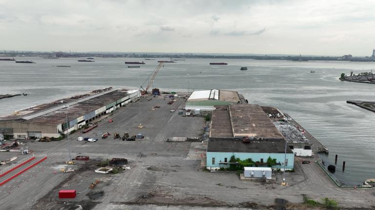 Low warehouse-like buildings sit in a parking lot on the end of a bay under a gray sky.