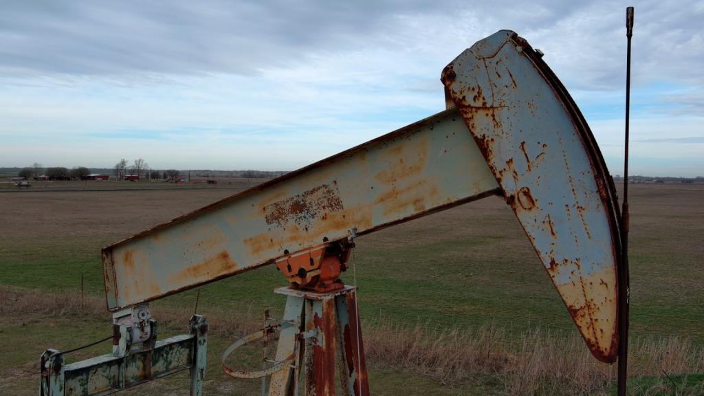 An old oil derrick sits on a yellowing field under a cloudy sky.