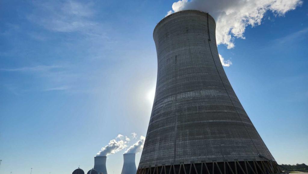 Tall concrete tower shaped like a funnel with white smoke coming out of top.