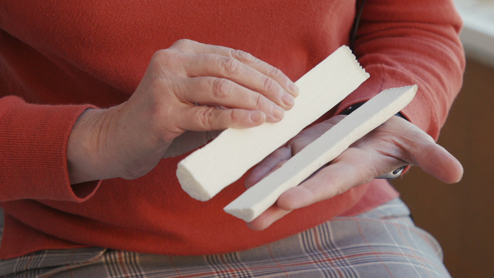 a person holds a white stick split in half with bands along the long inner cut