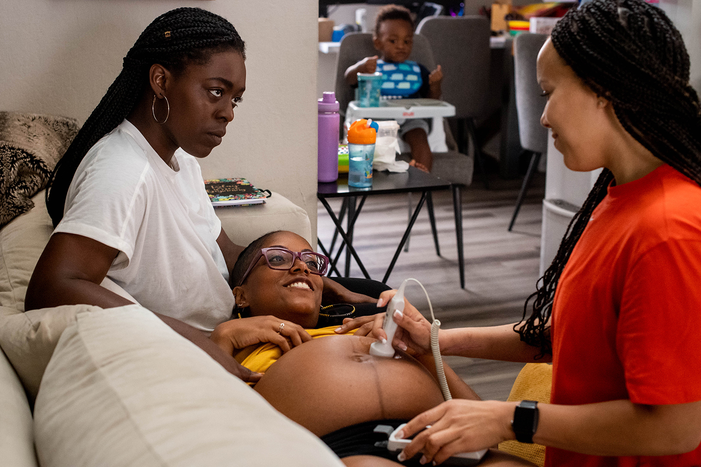 a pregnant woman is being attended to by two other women, one of whom is using a monitoring device on the pregnant woman's belly