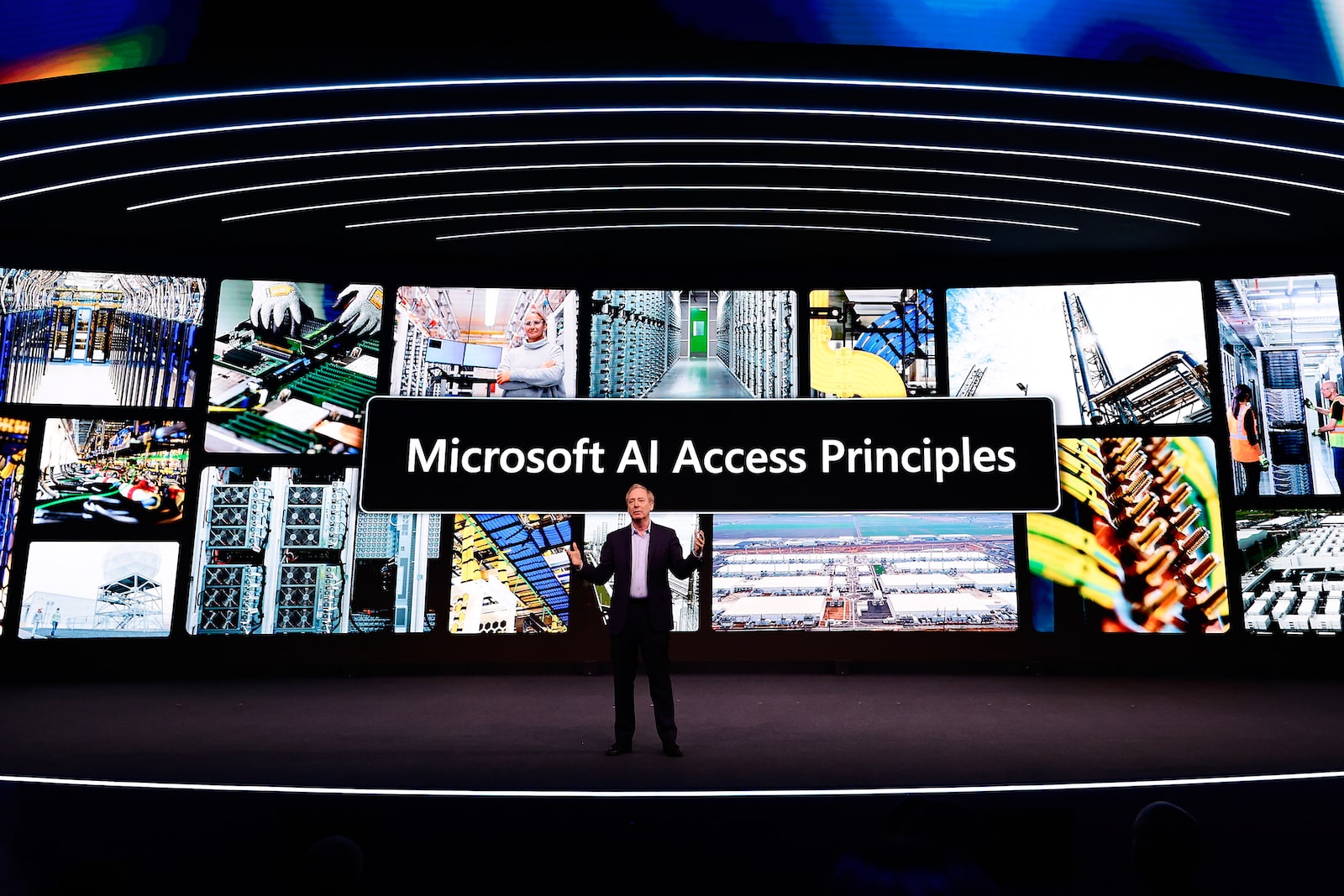 一名身穿西装的男子站在舞台上，屏幕前写着“微软人工智能接入原则”，背景是许多小型行业照片
