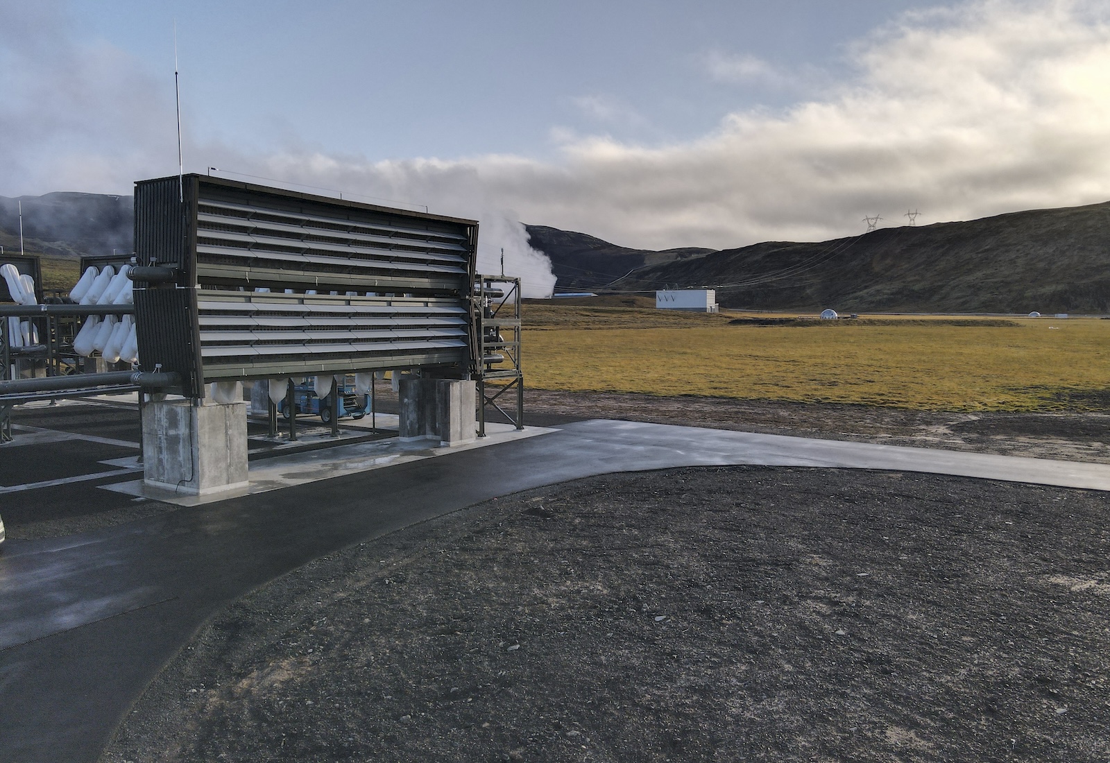 Rectangular direct air capture facility with built-in fans sits on cement with green hills in background.