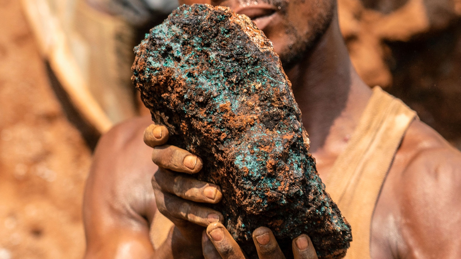 A man with muddy hands holds a huge brownish green rock.