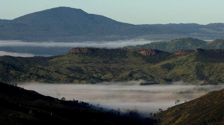 Fog threads through green and brown mountain ranges.