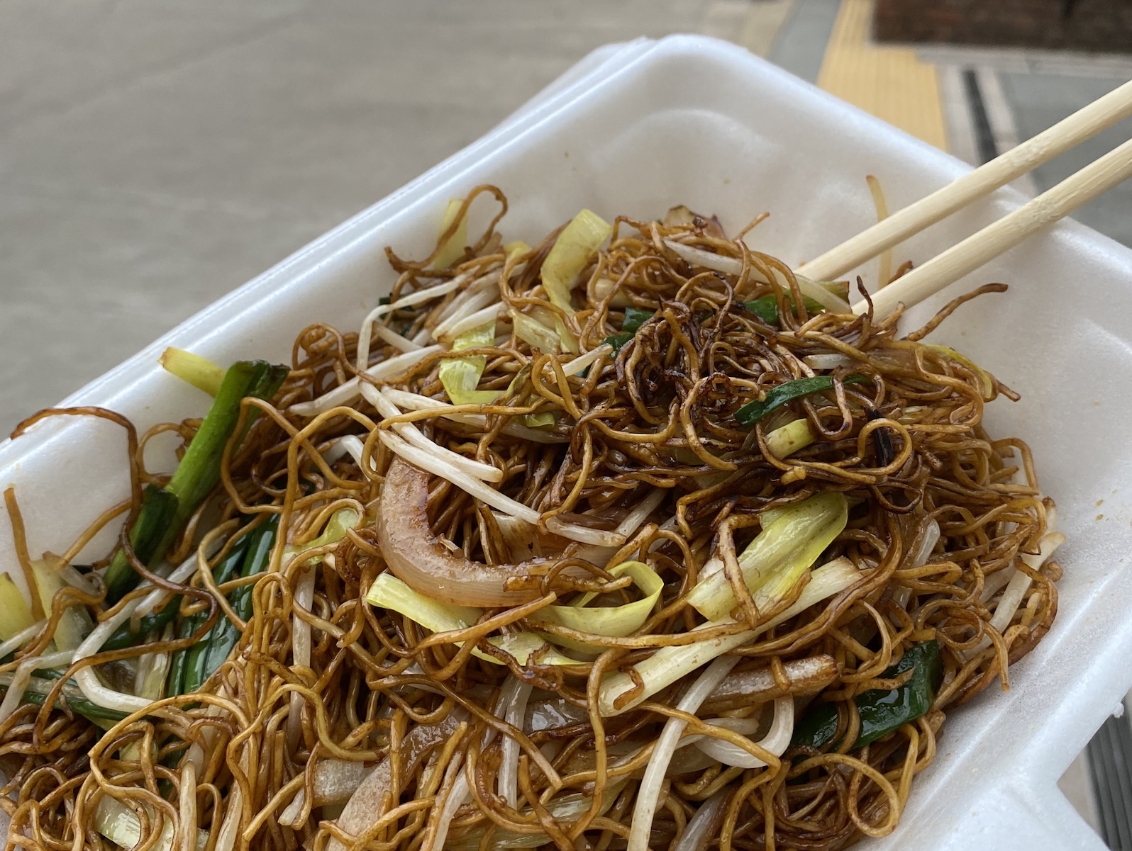 A white container filled with crispy blackened stir fry noodles