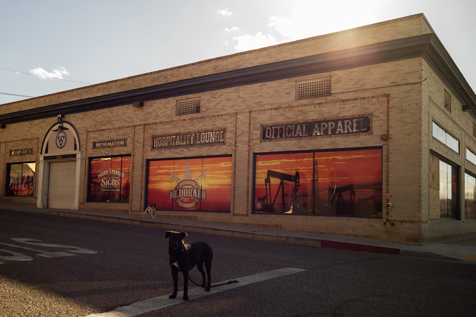 A dog stands outside of a brick building with pumpjack decorations