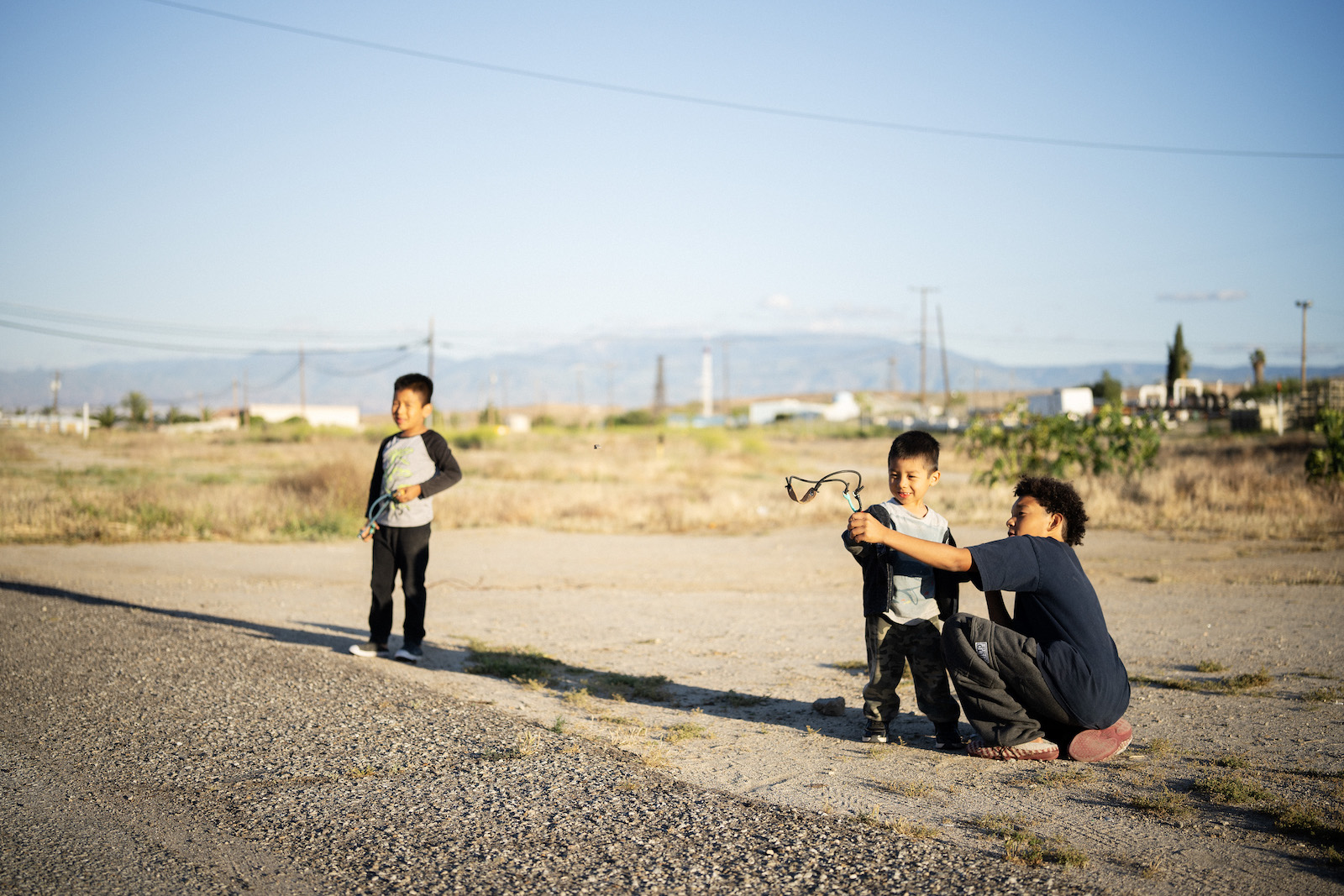 Three kids play with slingshots near rolling dirt hills