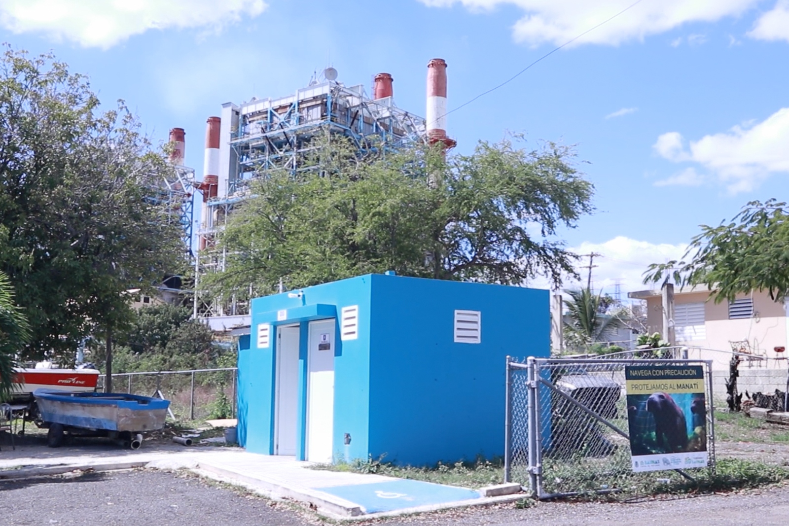 A small blue building sits in front of a large industrial complex with cooling towers.